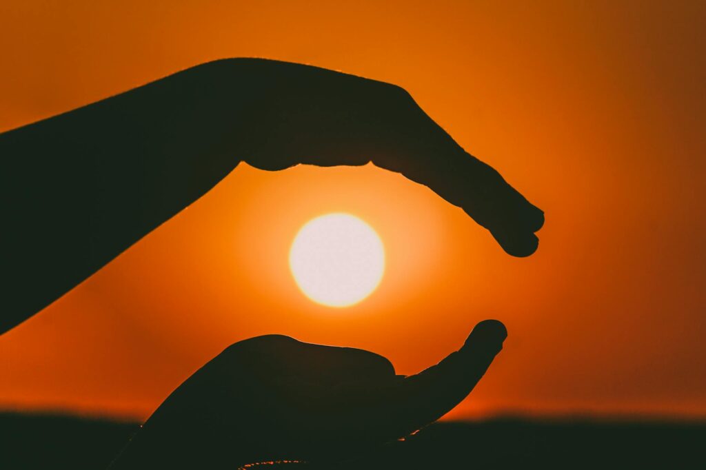 Silhouetted hands in a sunset scene capturing the sun's glow.